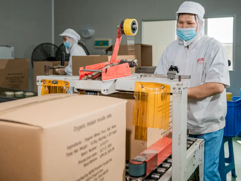 Kimdee workers packing seasoning packets with noodles and putting them into cartons